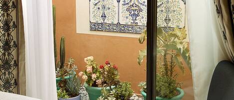 A room with a view of a courtyard, featuring a table, two chairs, a patterned rug, and potted plants.