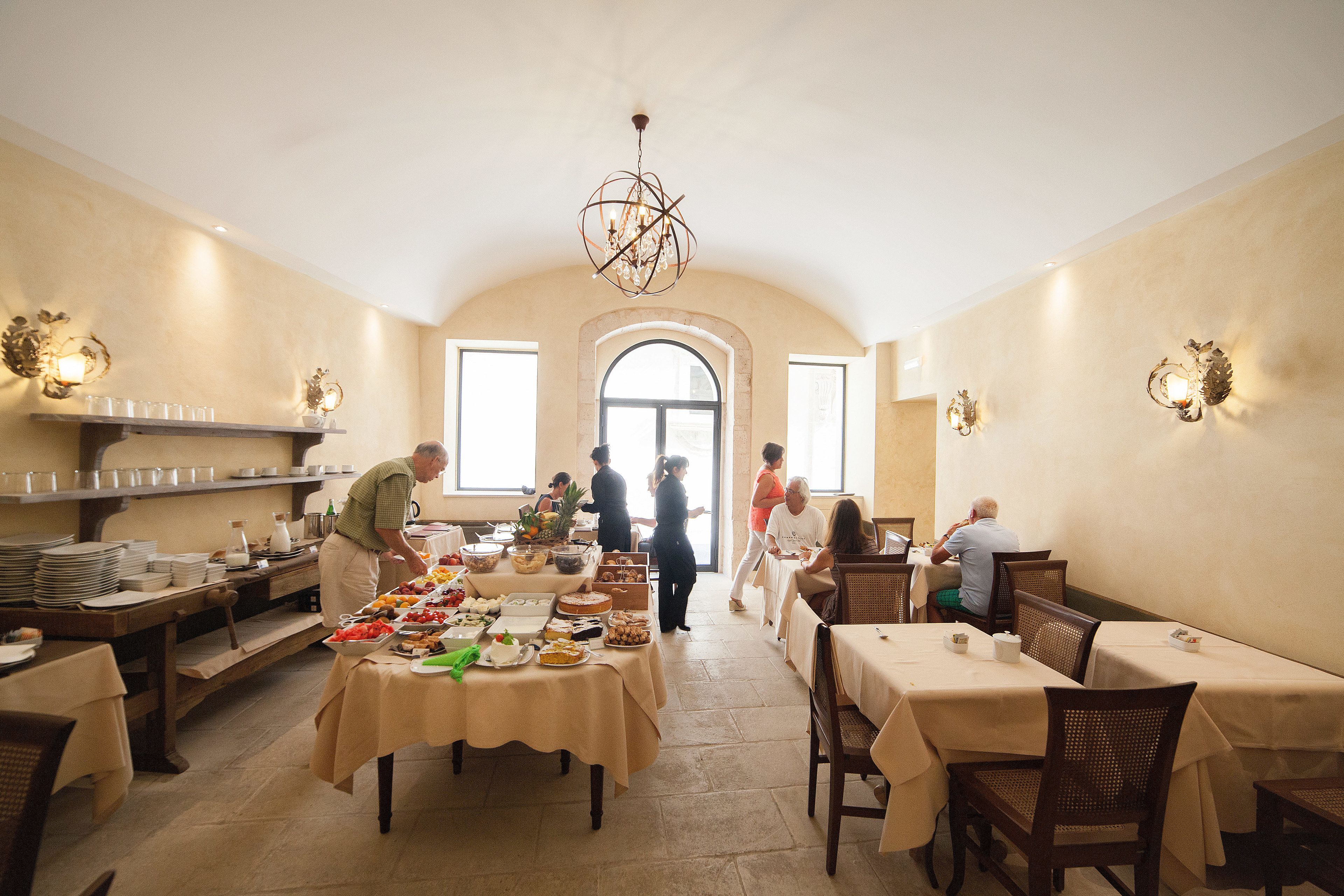 A dining area with tables set for guests, a buffet line, and a large arched window.