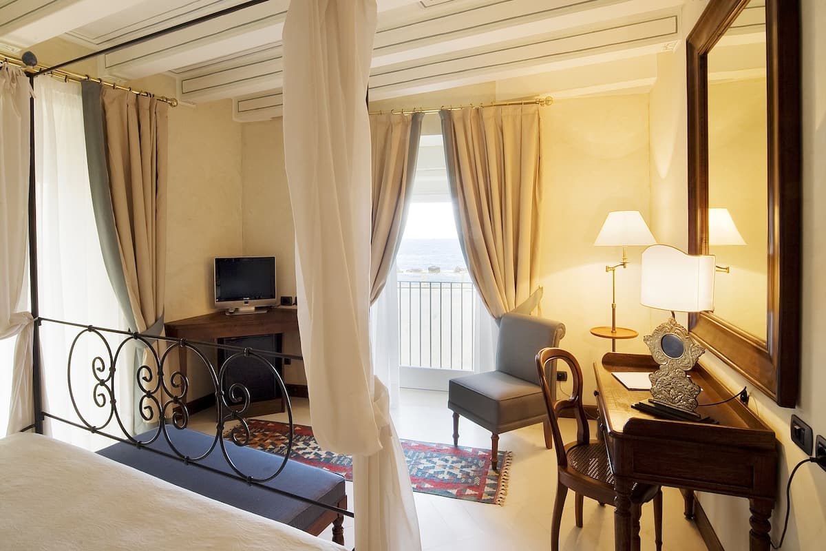 Habitación de hotel con cama, escritorio con televisor, silla, lámpara y un espejo grande.