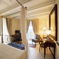 A hotel room with a bed, a desk with a TV, a chair, a lamp, and a large mirror.
