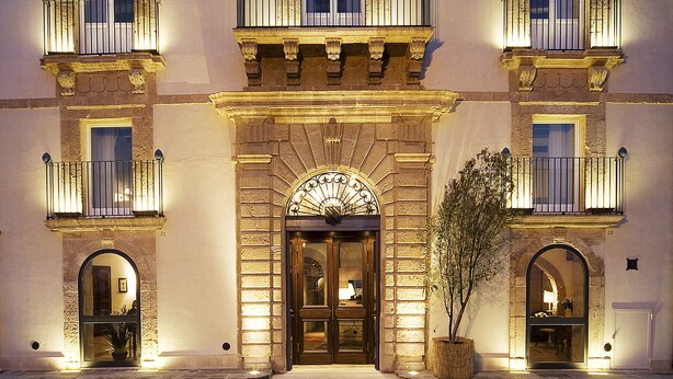 Un edificio histórico con entrada central, varios balcones y una planta grande en maceta al frente.