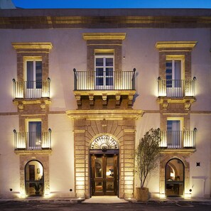 A historic building with a central entrance, multiple balconies, and a large potted plant in front. - Algila' Ortigia Charme Hotel (Syracuse)