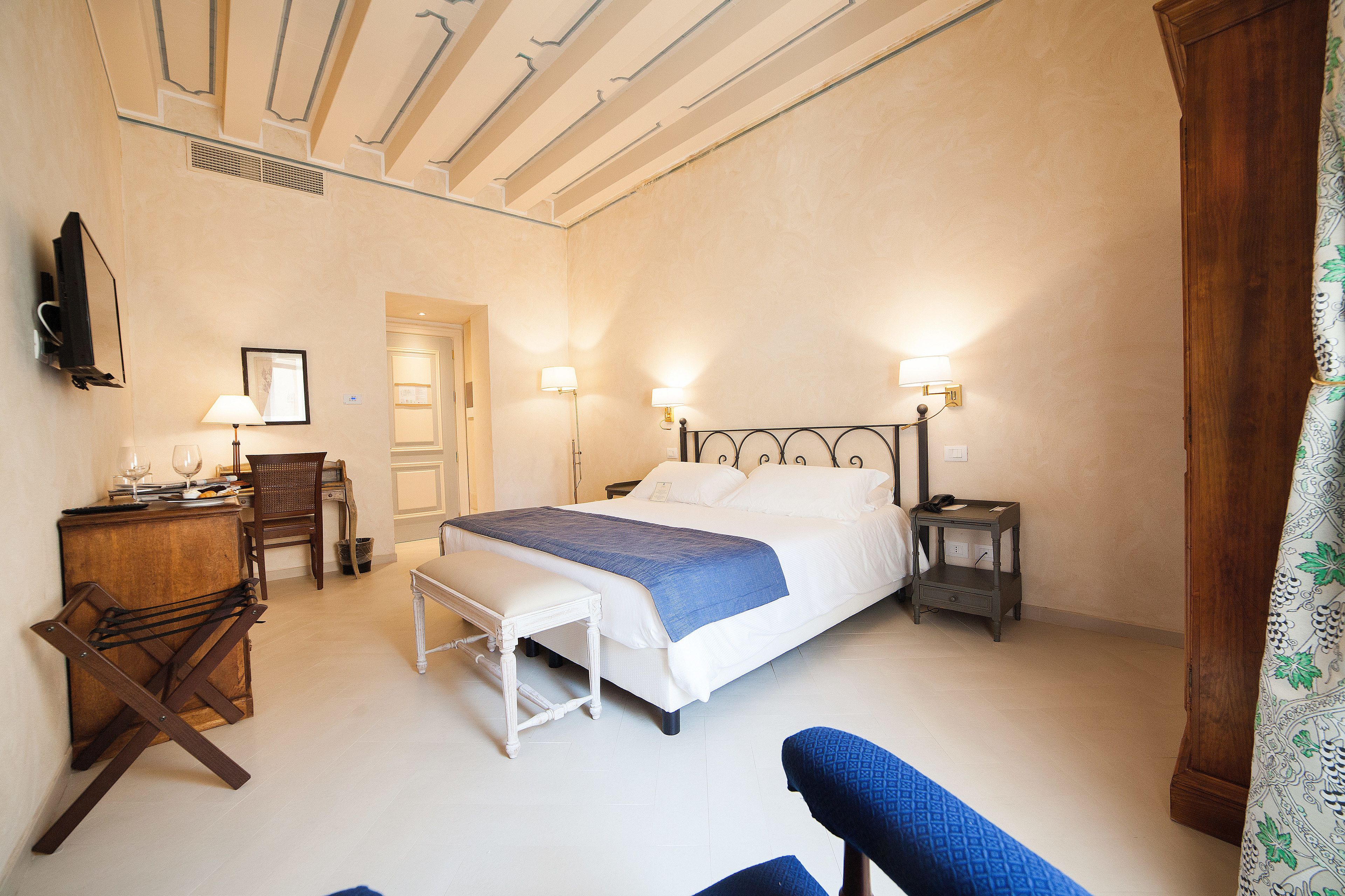 A bedroom with a bed, bedside tables, a desk, a chair, and a television.