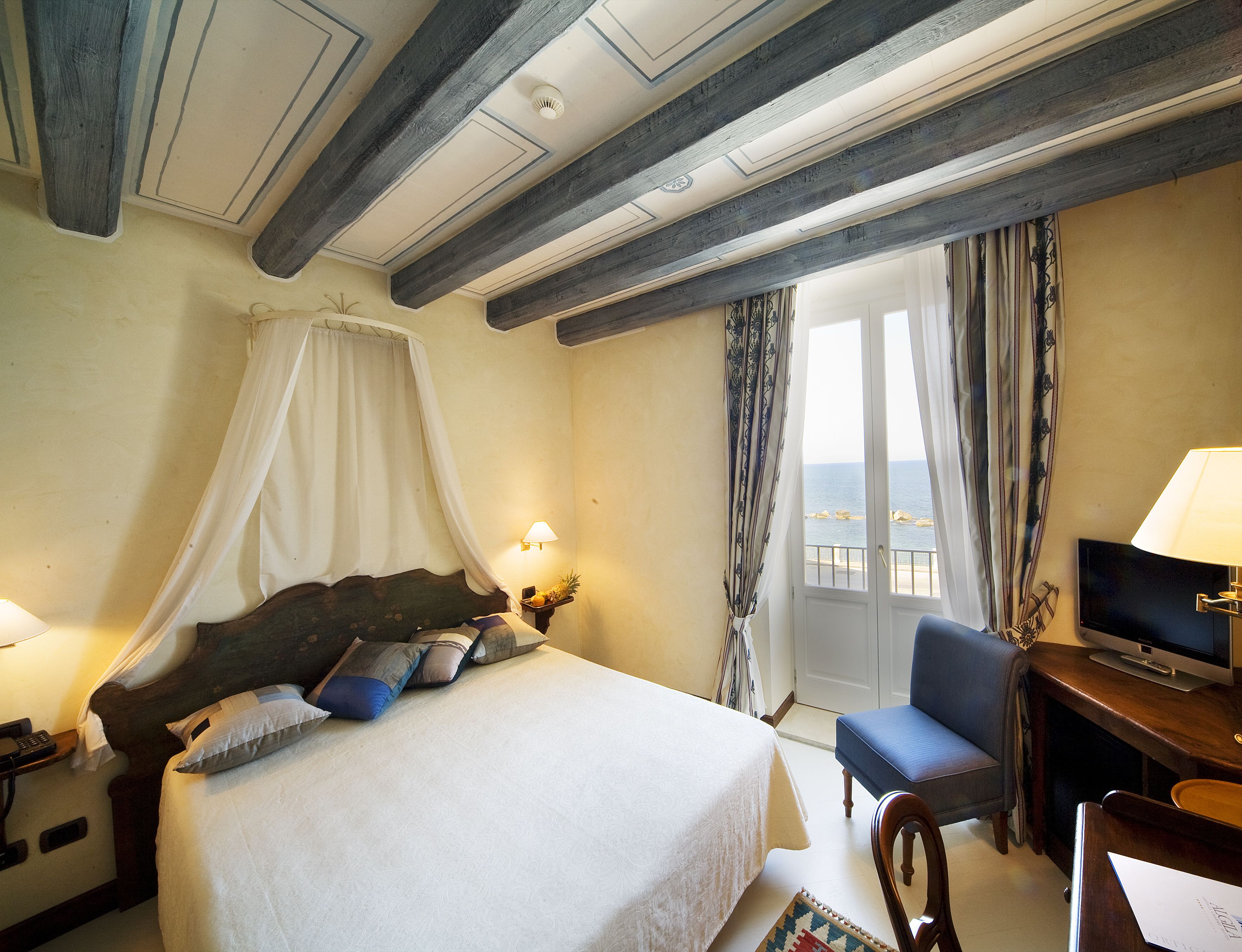 A hotel room with a bed, a desk with a television, a chair, and a window with curtains.