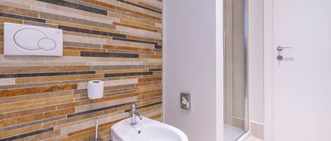 Une salle de bain dotée d’un revêtement mural moderne en carreaux, d’un bidet, d’un porte-rouleau de papier toilette et d’un espace douche.