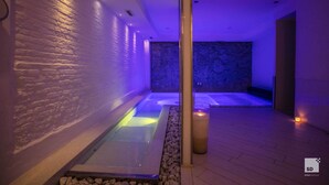 A spa area with a hot tub and a massage table, surrounded by stone walls and a wooden floor.