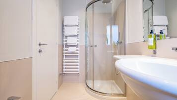 Un baño moderno con ducha envuelta en vidrio, un lavabo blanco y un perchero con varias toallas.