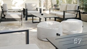 An outdoor seating area with modern furniture, including sofas and a coffee table, under a shaded canopy.