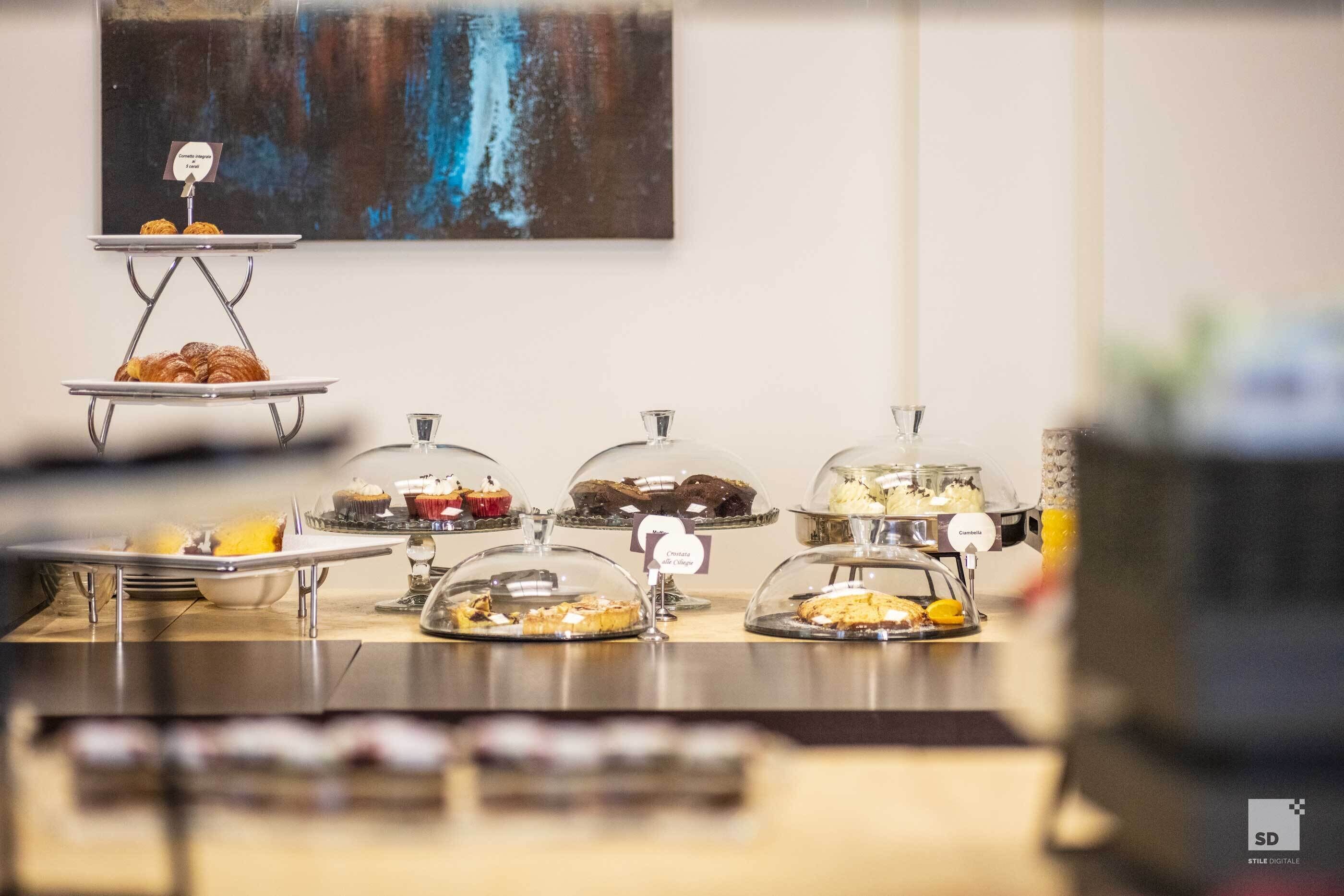 Un bufé con diversos alimentos bajo campanas de vidrio, un letrero que indica 'Cocina Contemporánea' y un cuadro en la pared.