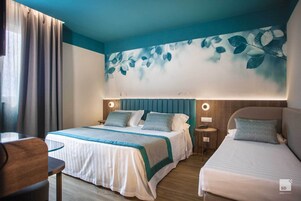 A hotel room with a bed, a desk, and a wall mural.