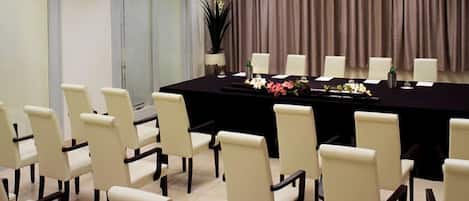 A conference room with a long table, white chairs, and a curtain backdrop.