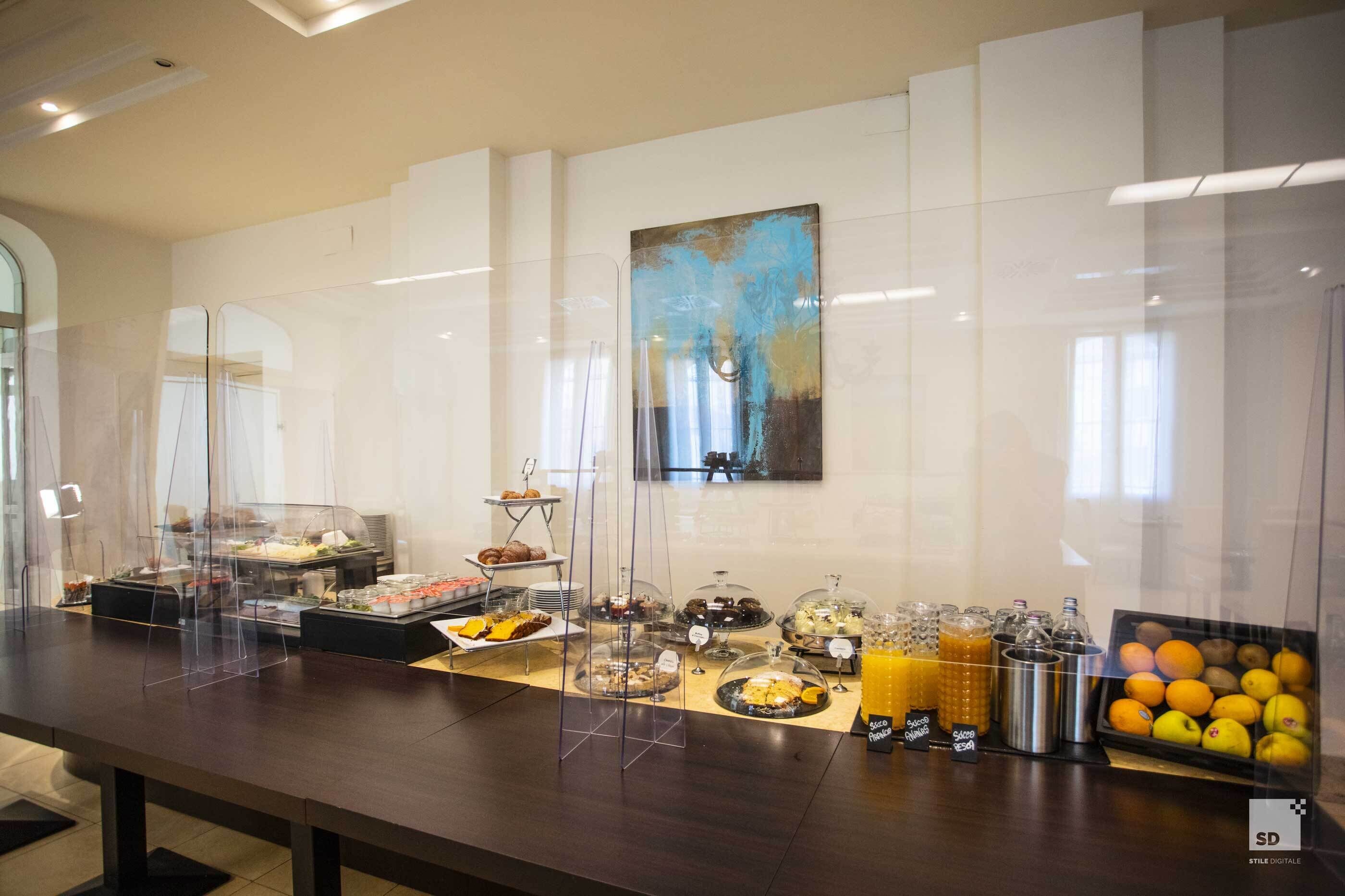 Un'area buffet con diverse pietanze e bevande, tra cui frutta e pasticceria, esposte in contenitori trasparenti.