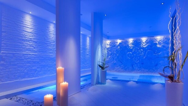 A spa area with a stone wall, candles, a water feature, and potted plants.
