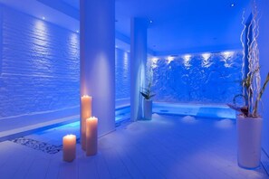 Un área de spa con pared de piedra, velas, fuente de agua y plantas en macetas.