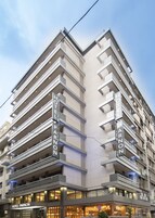 Ένα πολυώροφο ξενοδοχείο με μπαλκόνια και μια επιγραφή που γράφει «ΞΕΝΟΔΟΧΕΙΟ ΠΑΡΝΩΝ».
