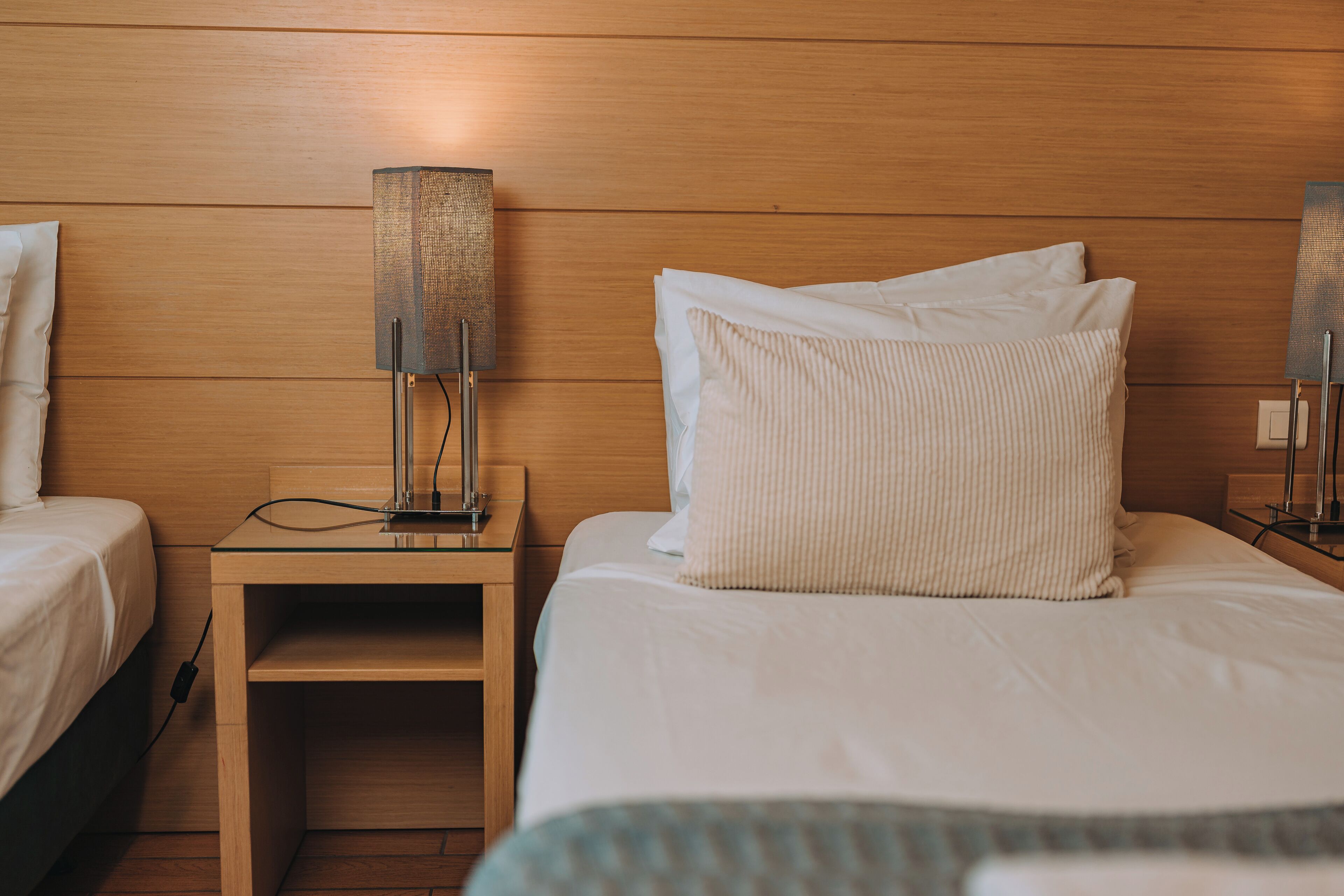 A hotel room with two beds, a nightstand with a lamp, and a power outlet.