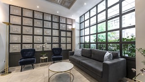 A modern living room with a grey sofa, two armchairs, a round coffee table, and a large window with a city view. - Parnon Hotel (Athens)