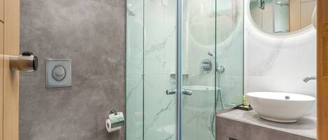 Une salle de bain moderne avec une douche en verre, un lavabo blanc et un mur recouvert de carreaux de marbre.