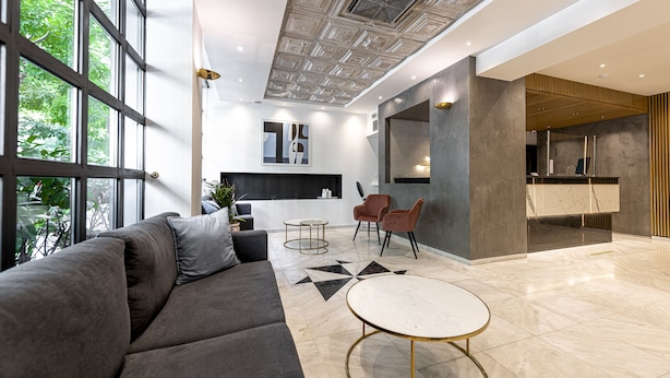 A modern interior with a gray sofa, round tables, and a kitchen area with a countertop and chairs. - Parnon Hotel (Athens)