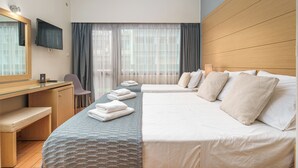 A hotel room with a wooden desk, a flat-screen TV, a large bed with white linens, a smaller bed, a chair, and a window with curtains. - Parnon Hotel (Athens)