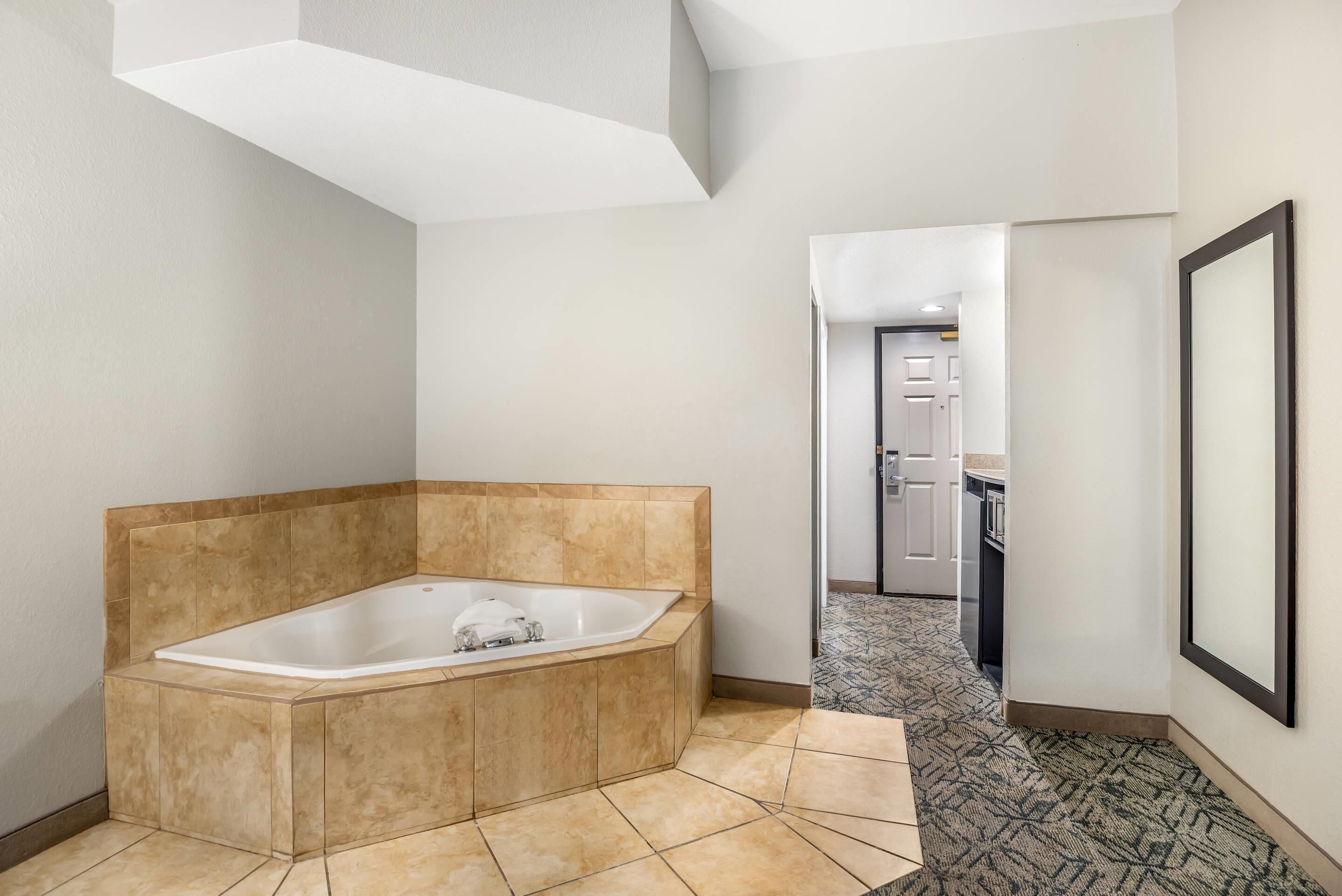 A modern bathroom with a freestanding bathtub, a patterned hallway, and a door leading to a kitchen area.