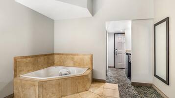 A modern bathroom with a freestanding bathtub, a patterned hallway, and a door leading to a kitchen area.