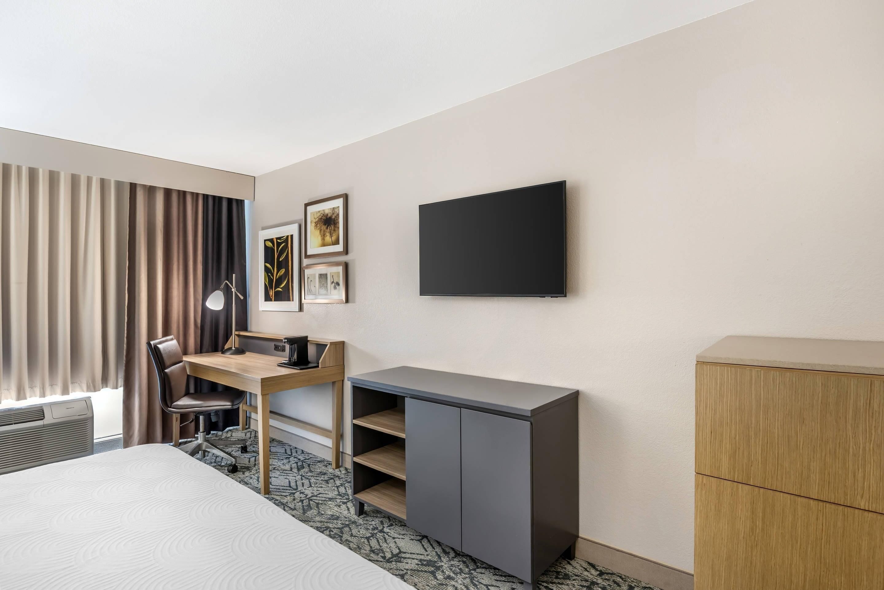 A hotel room with a bed, desk, chair, TV, and wardrobe.