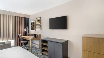 A hotel room with a bed, desk, chair, TV, and wardrobe.