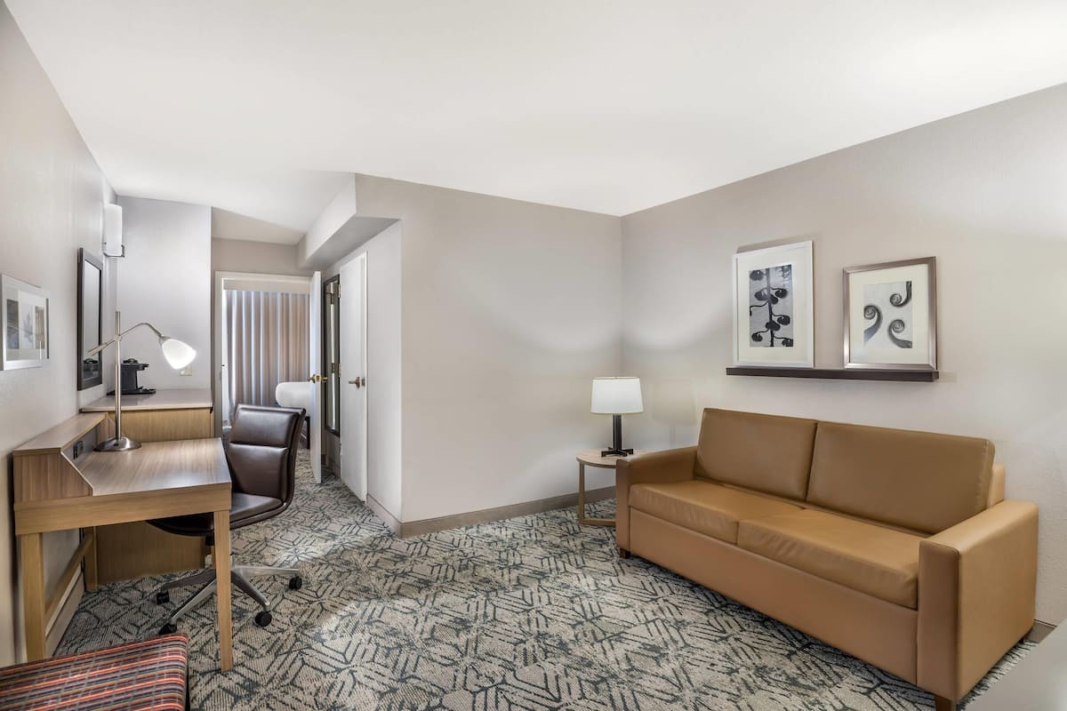 A hotel room with a desk, chair, sofa, and two wall-mounted lamps.