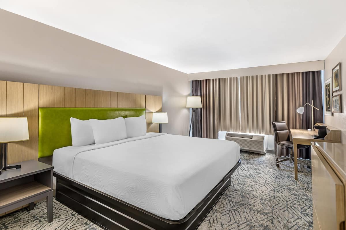 A hotel room with a large bed, a desk, a chair, a lamp, and a window with curtains.