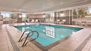 Une piscine dotée d’une terrasse carrelée, de chaises longues et offrant une vue sur l’extérieur.