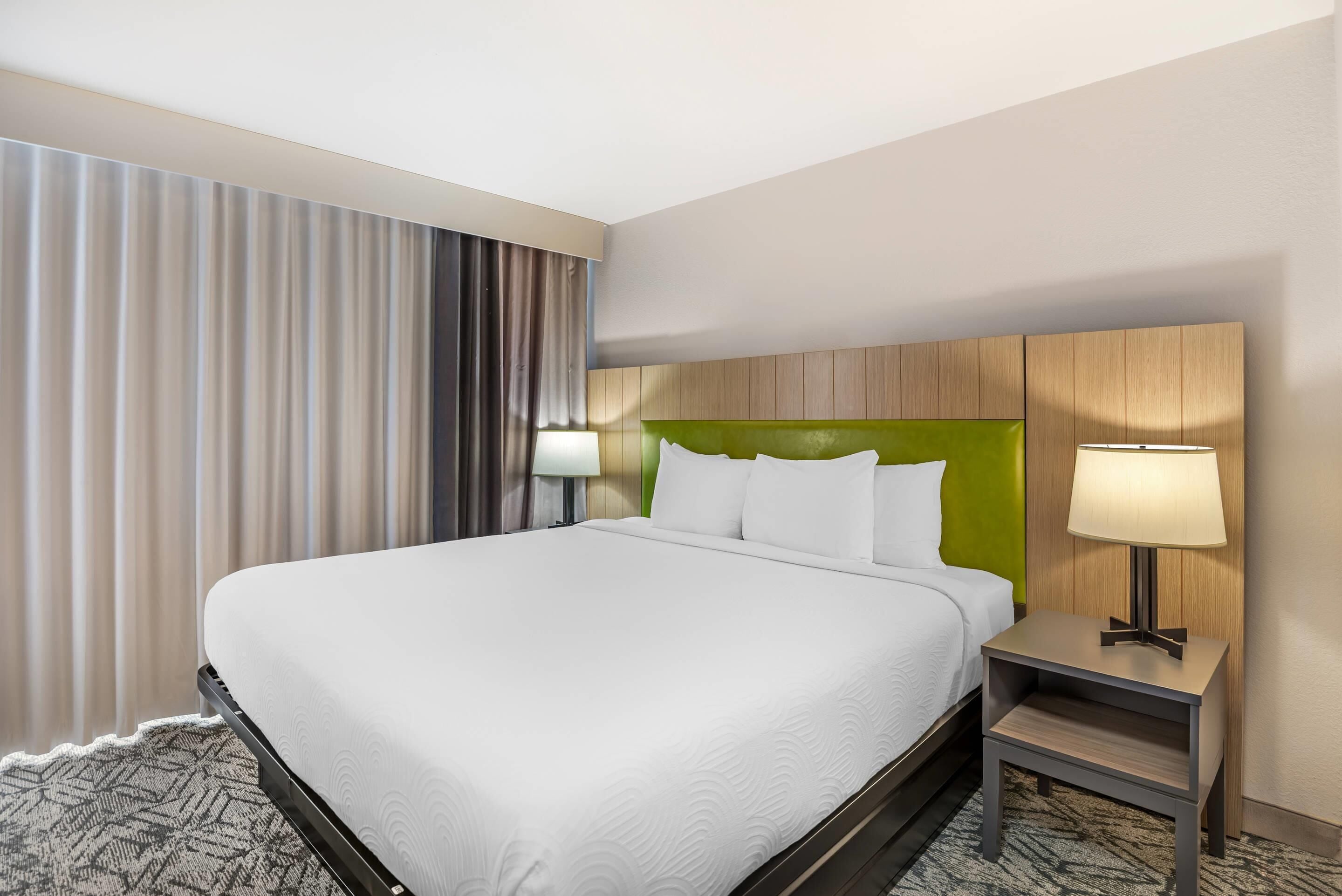 Une chambre d’hôtel avec un grand lit, deux lampes de chevet, une tête de lit et un sol recouvert de moquette.