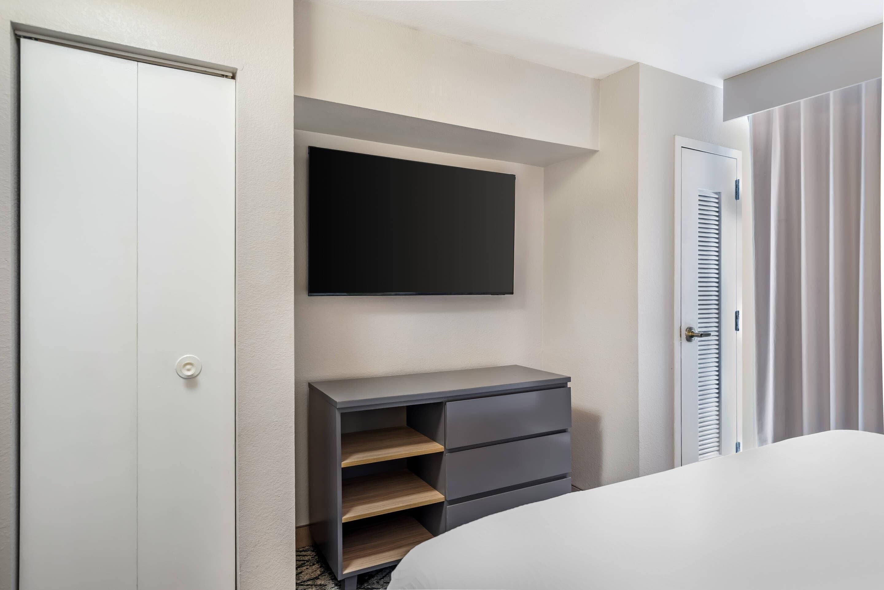 Quarto com cama, guarda-roupa, televisão na parede e mesa de cabeceira.