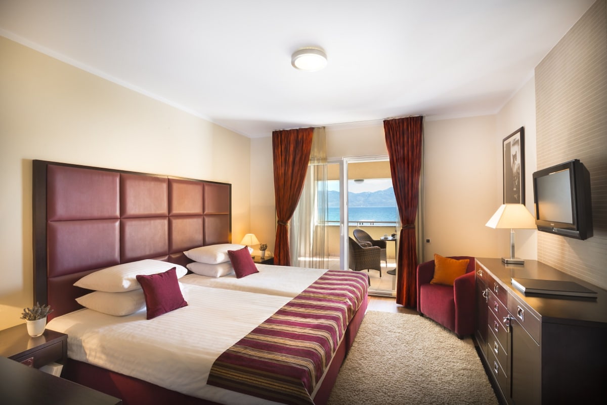 A hotel room with a large bed, a desk, a chair, a TV, and a balcony with a view.