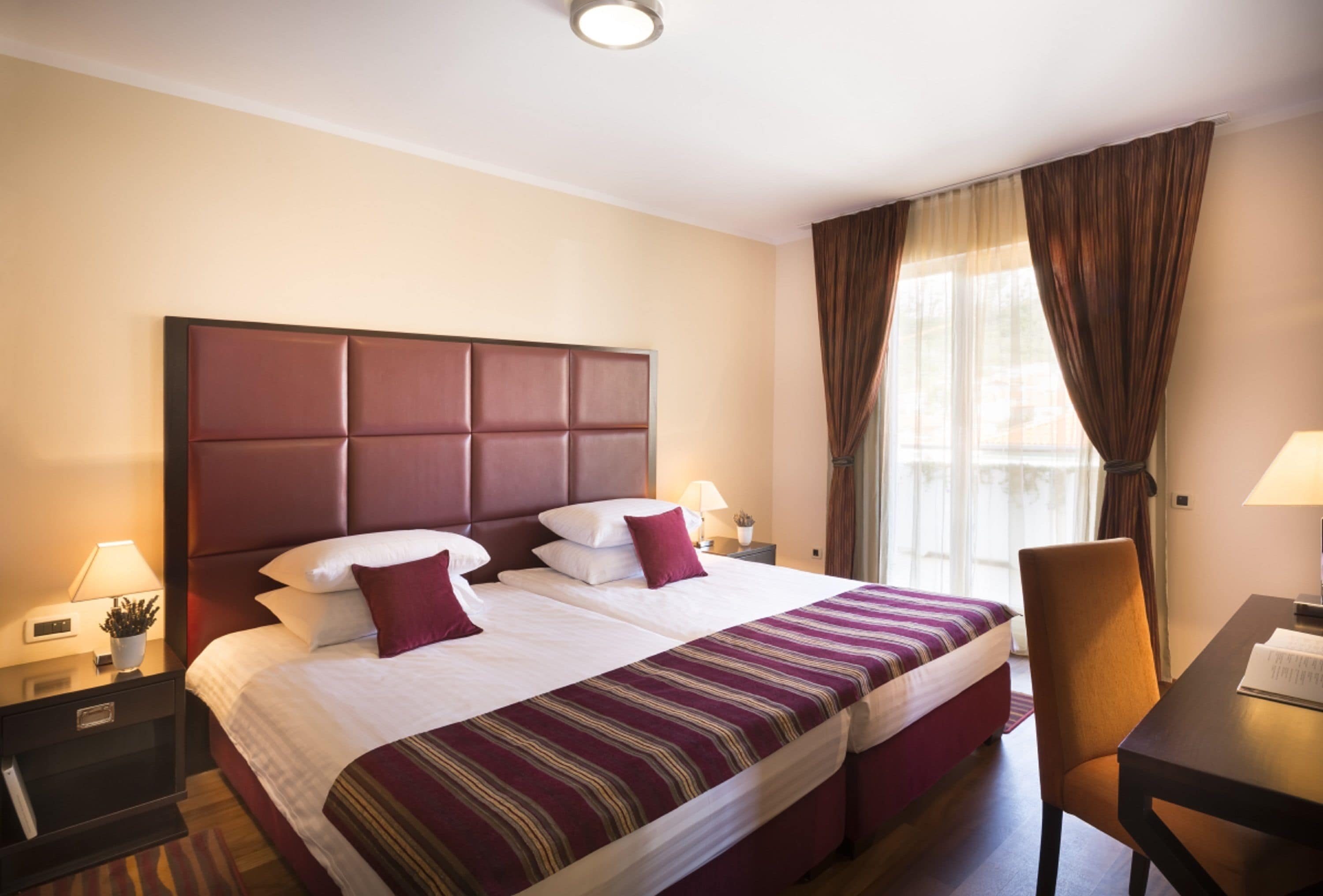 Une chambre d’hôtel avec un grand lit, deux tables de chevet, une chaise et une fenêtre avec des rideaux.