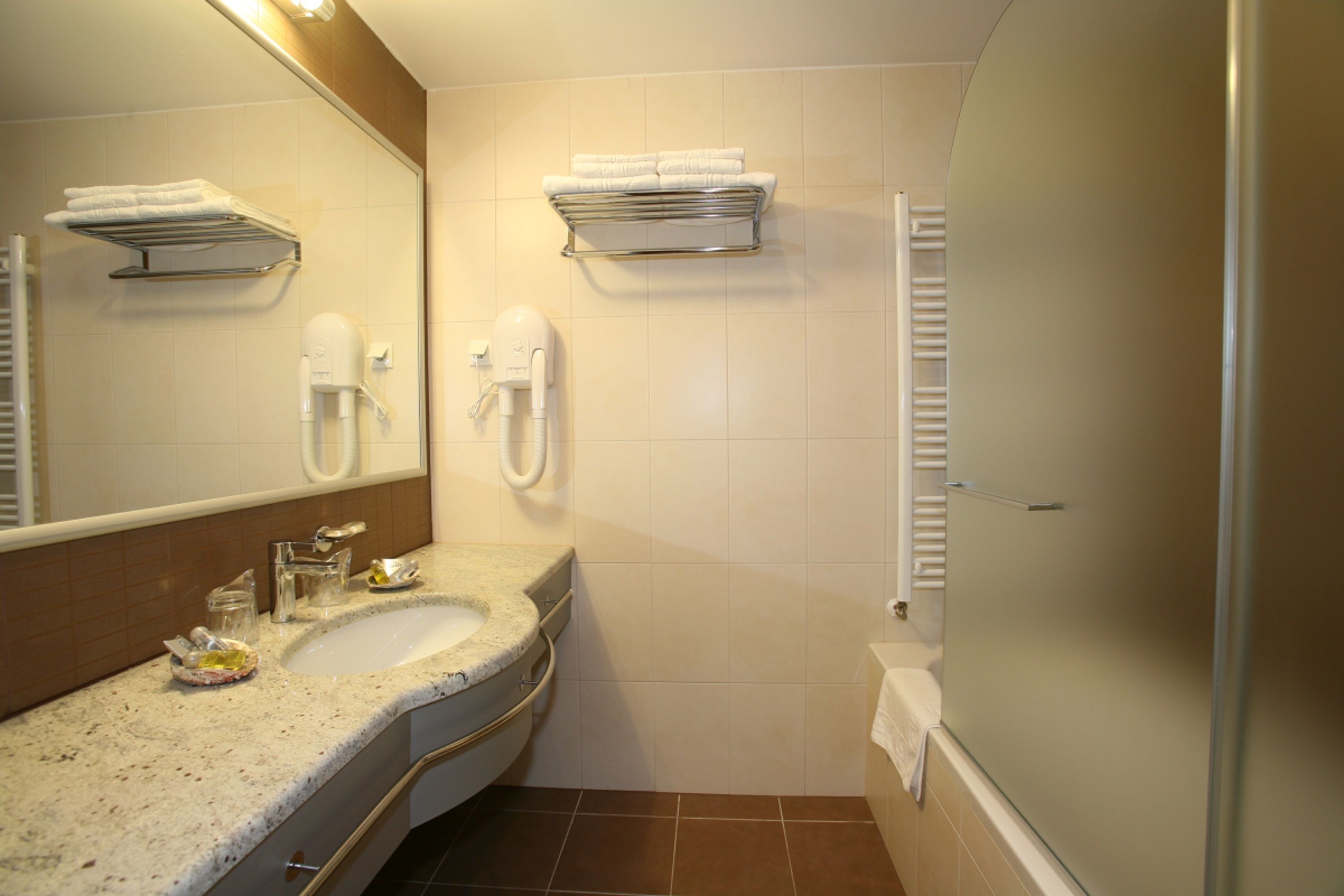 A bathroom with a sink, mirror, towel rack, and a shower area.