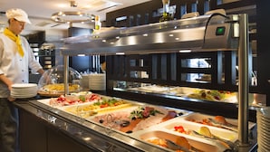 Zona de bufé con diversas opciones de comida, como carnes, quesos y verduras, en un ambiente de cocina moderna.
