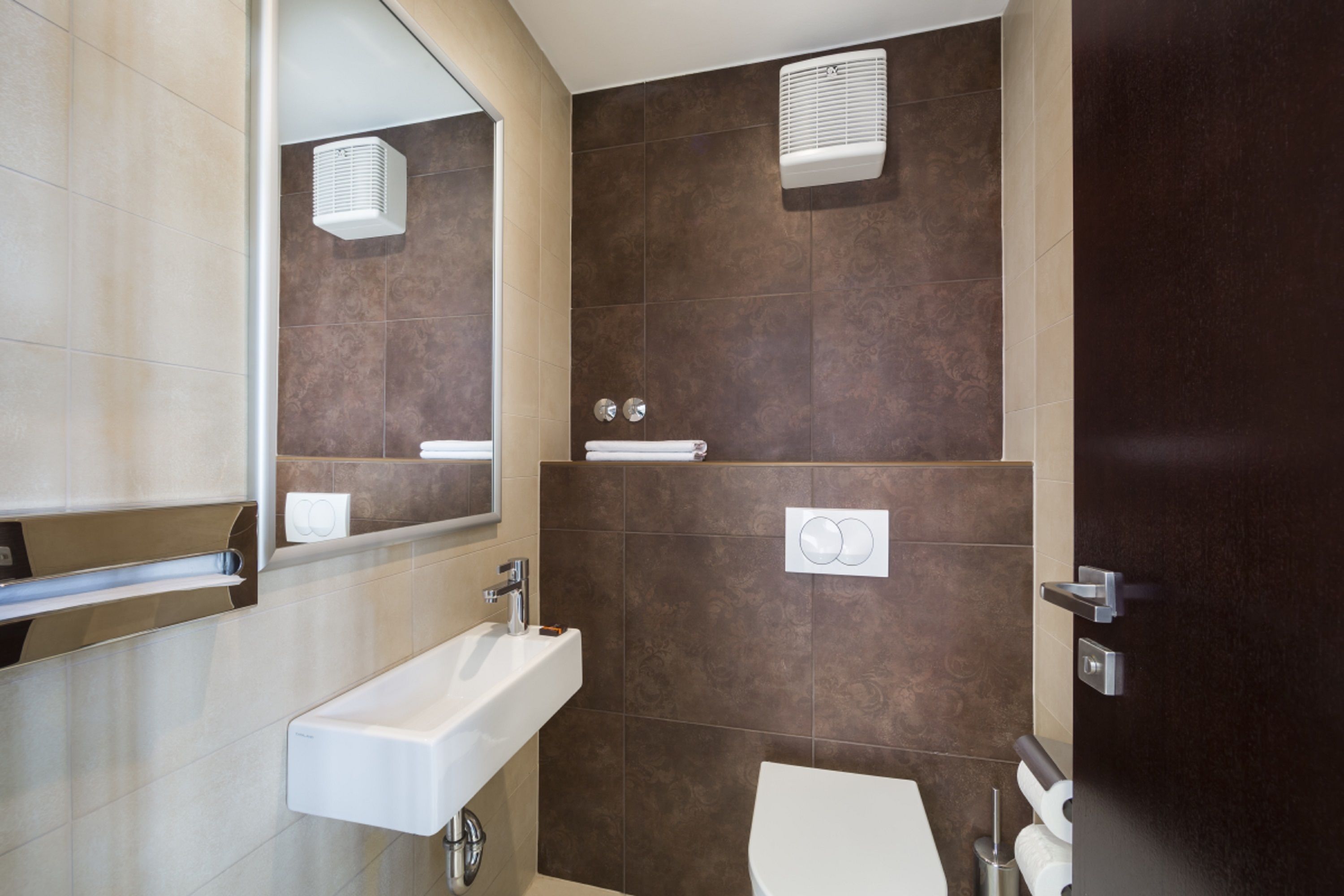 A modern bathroom with a white sink, a mirror, a towel rack, and a toilet.