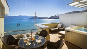 Un balcón con mesa lista para el desayuno, un jacuzzi y vistas al mar.