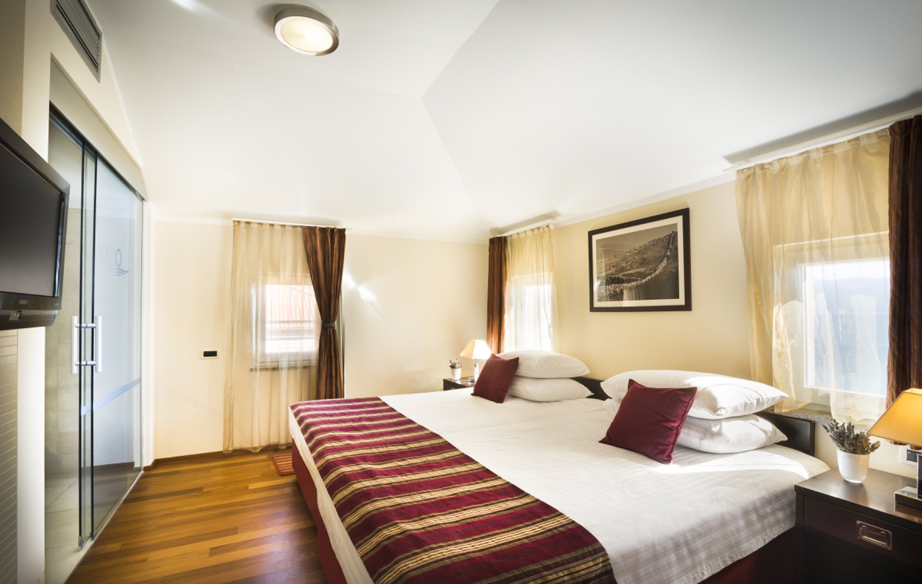 Une chambre d’hôtel avec un grand lit, une télévision, une table de chevet avec une lampe et une fenêtre avec des rideaux.