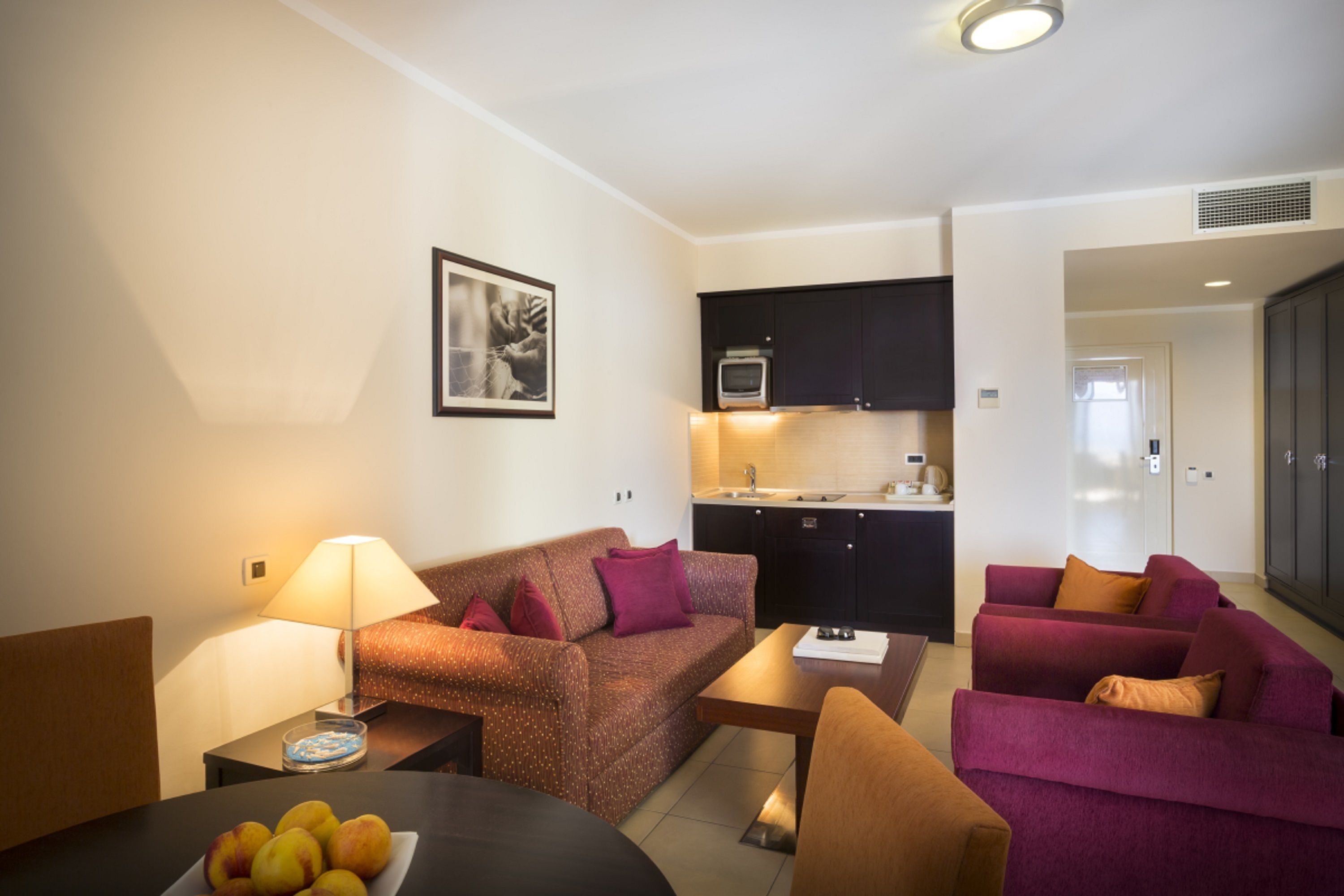 A compact living space with a kitchenette, a sofa, a dining table, and a lamp.