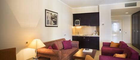 A compact living space with a kitchenette, a sofa, a dining table, and a lamp.