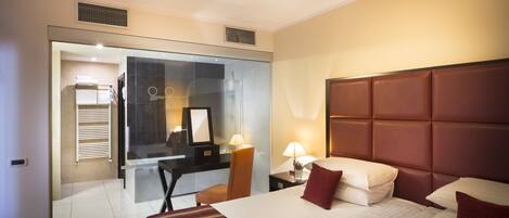Une chambre d’hôtel avec un grand lit, un bureau et une cloison en verre qui sépare la chambre d’une salle de bain.