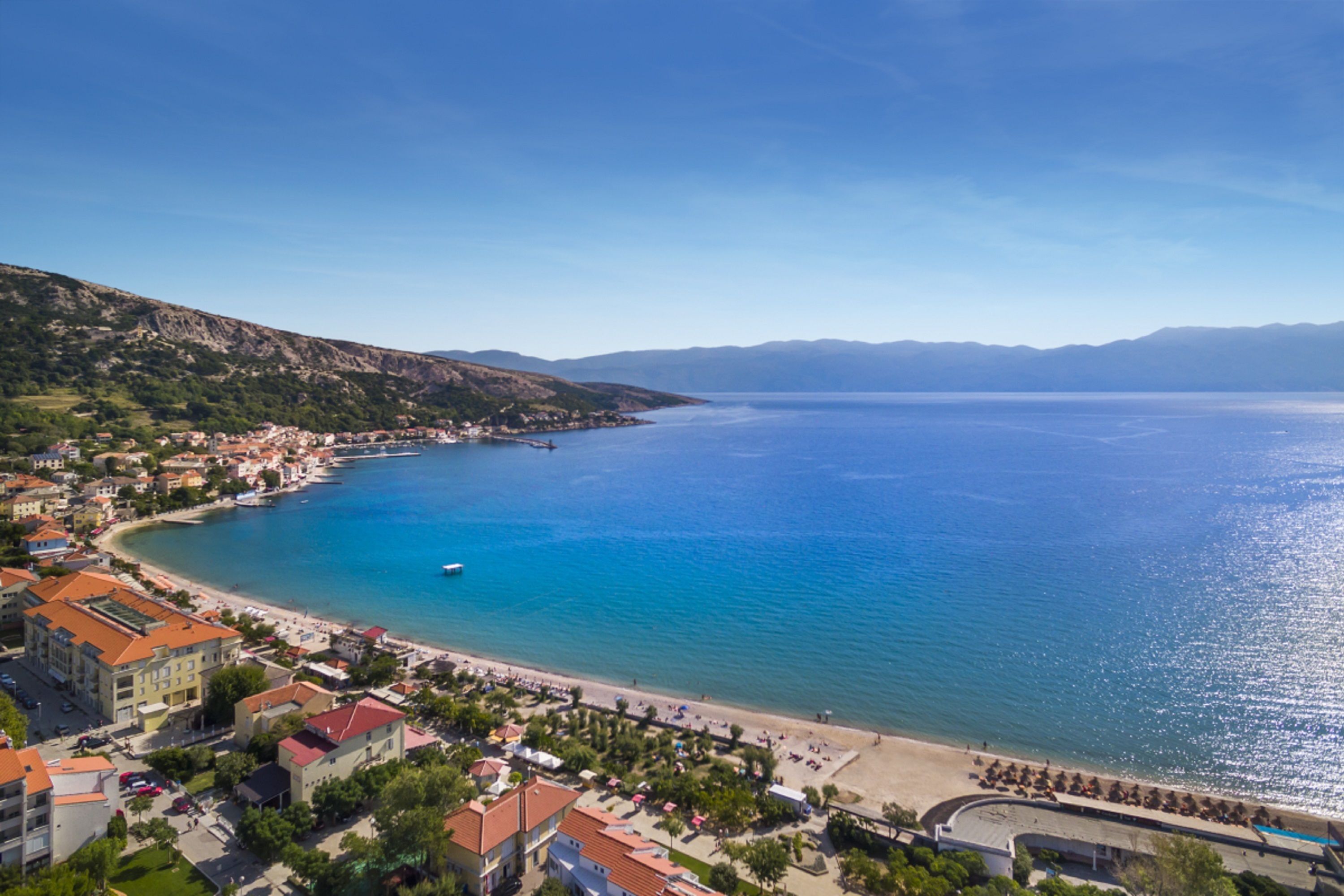 Eine Küstenstadt mit Strand, Gebäuden und einem klaren, blauen Meer.