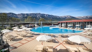 Un área de piscina con sillones de descanso y sombrillas, rodeada de montañas.