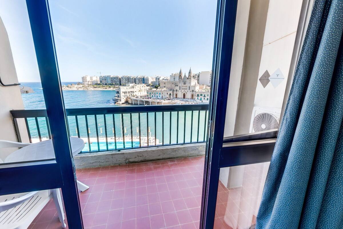 A balcony with a view of a coastal cityscape, including a church and residential buildings.