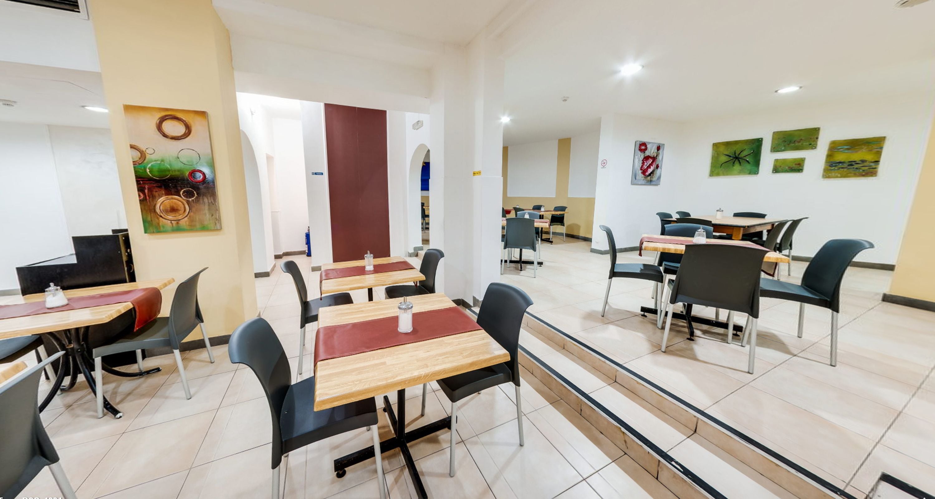 Una sala da pranzo moderna con diversi tavoli e sedie, una scala e opere d'arte alle pareti.