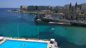 A coastal cityscape with a prominent church, a marina with boats, and a swimming pool area. - St Julian's Bay Hotel (St. Julian's)