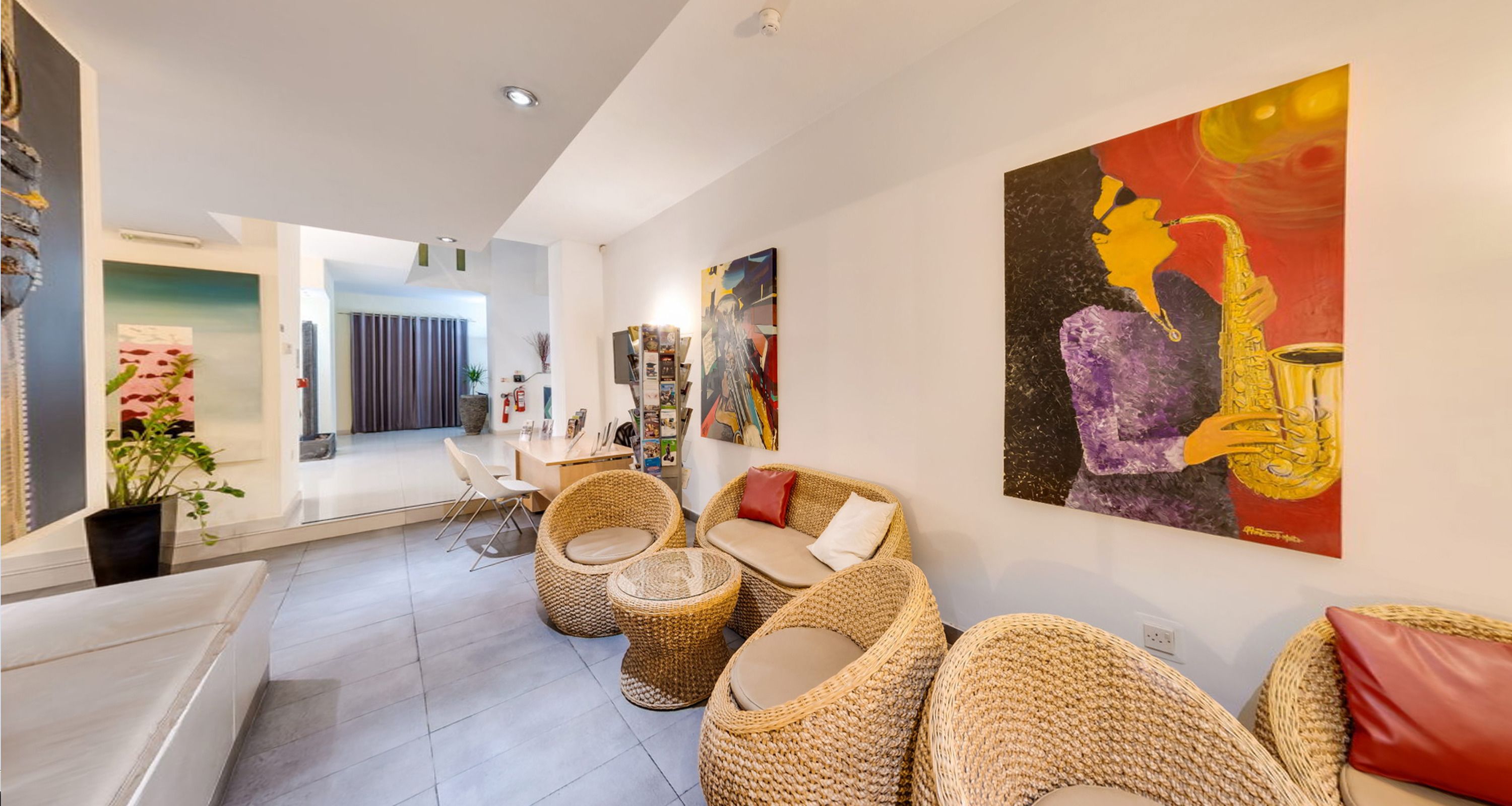 Een moderne woonkamer met rieten meubels, een bank en een salontafel. Op de muur hangt een schilderij van een saxofoon.