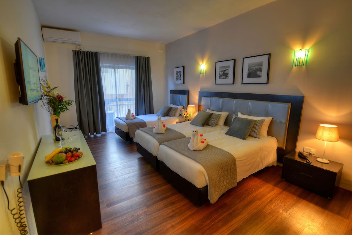 A hotel room with two beds, a desk with a fruit bowl, and a TV on the wall.